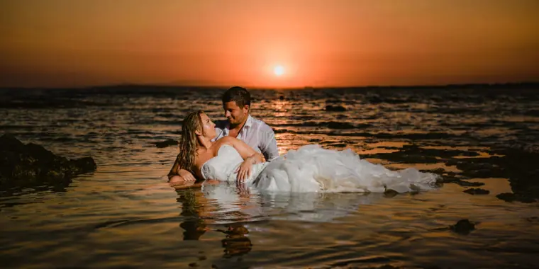 Couple lying in the shallow sea in wedding clothes at sunset