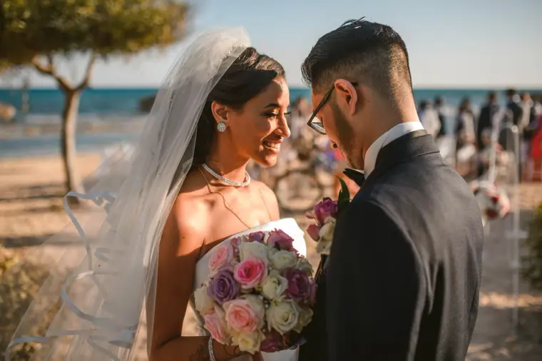 Newlyweds smiling at each other with the sea and guests behind, Ayia Napa