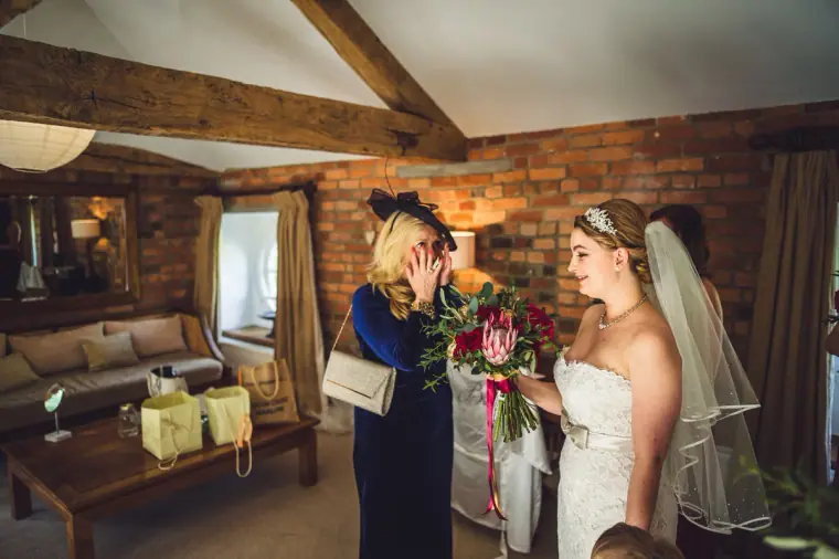 Woman in a navy fascinator wiping her eyes as she sees the bride