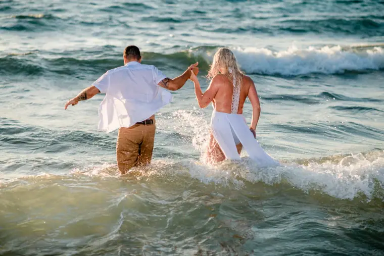 Bride leading the groom by the hand into the waves