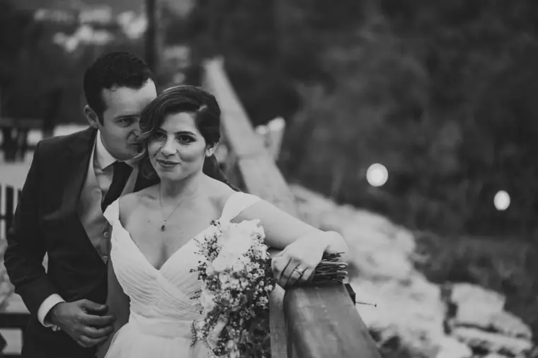 Black-and-white photo of the groom resting his head against the bride's