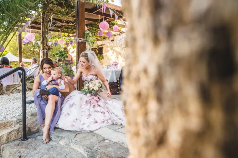 Bride in her floral gown sitting on stone steps with a bridesmaid and toddler