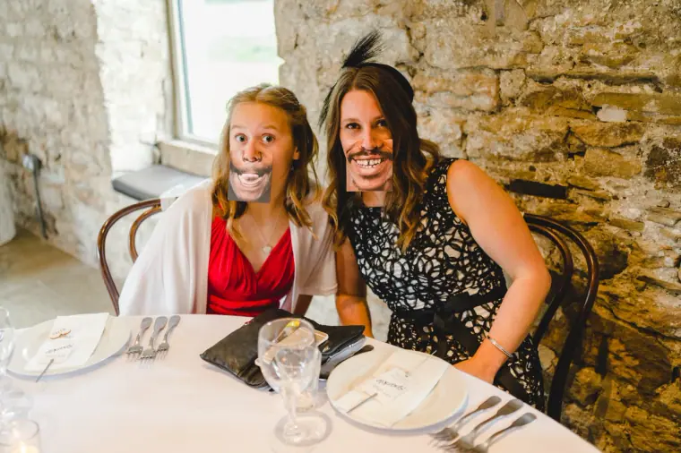 Two guests at a reception table holding mouth props up to their faces