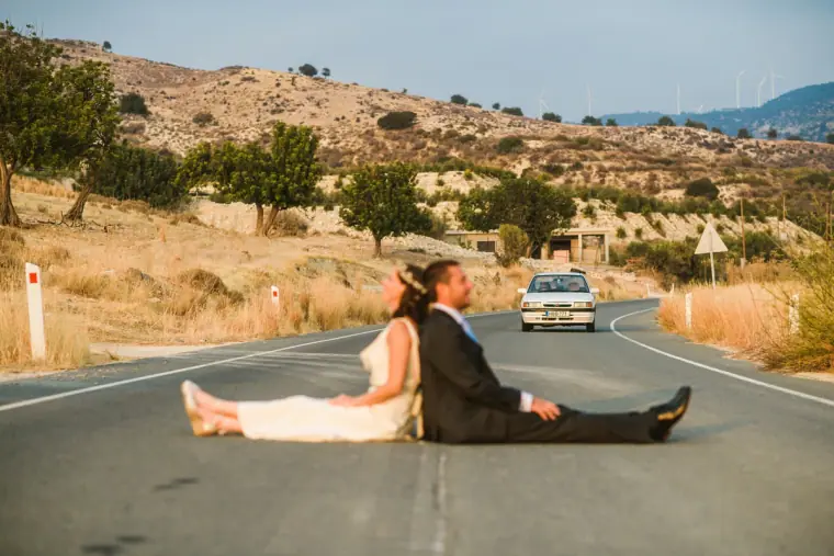 Newlyweds lounging on a mountain road as a car approaches in the distance