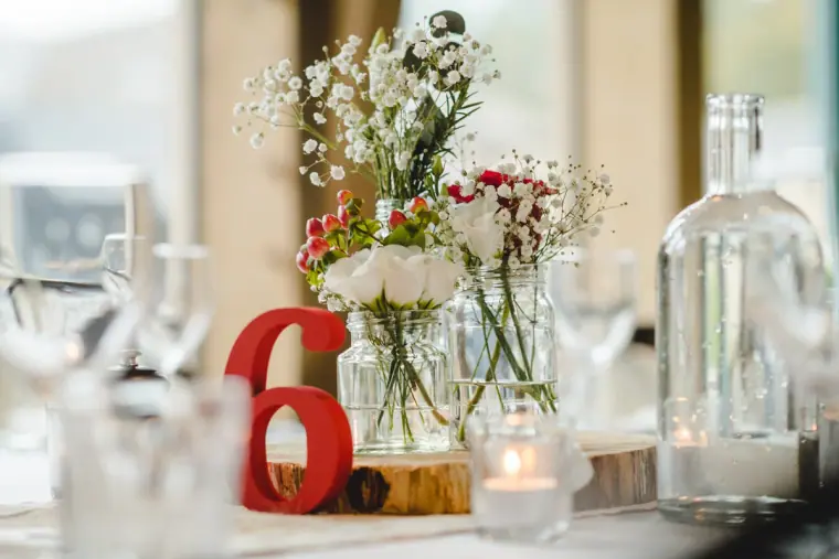 Table centrepiece of gypsophila and red flowers in glass bottles with a red table number 6