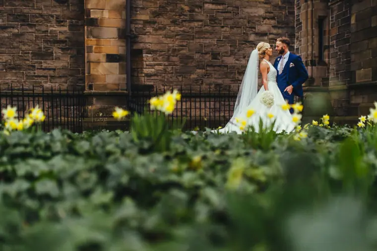 Bride and groom kissing behind a bed of daffodils outside the sandstone church