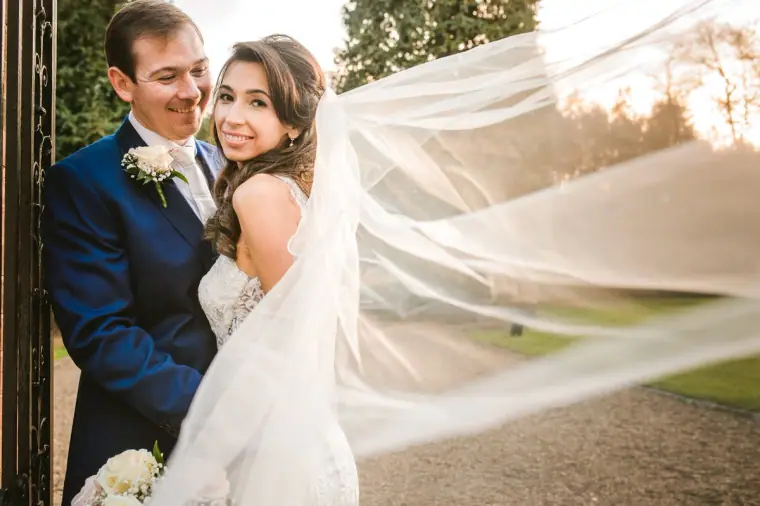Elina's long veil blowing in the breeze as she and Iain embrace at Wotton House