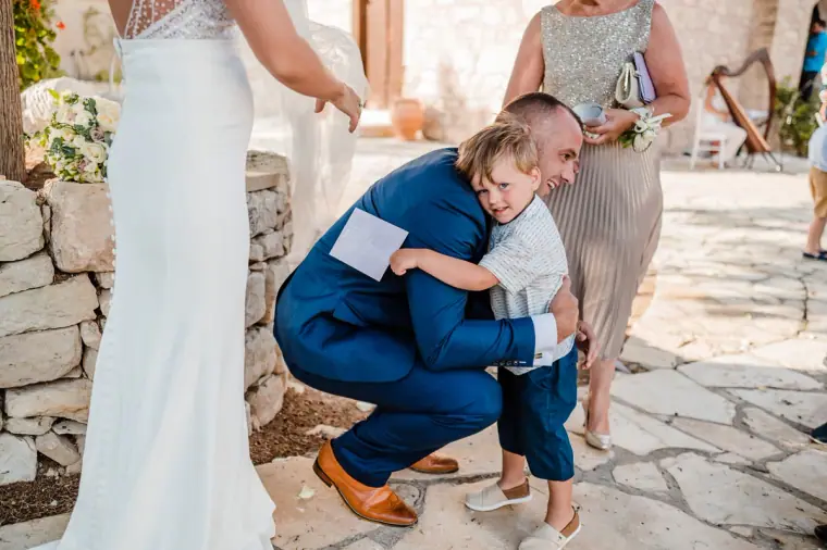 Groom crouching to hug a young boy in the courtyard after the ceremony