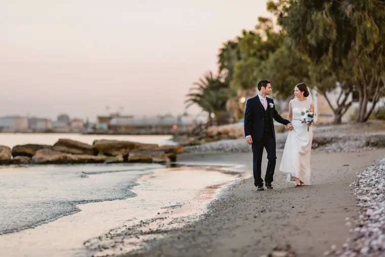 Bride and groom strolling along a sandy shoreline at dusk