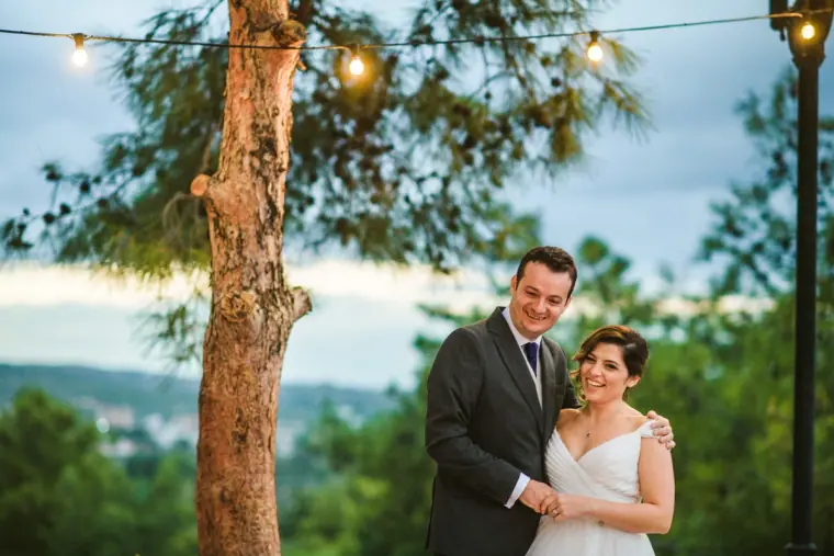 Nermine and Christopher smiling together beside a pine trunk with hills behind