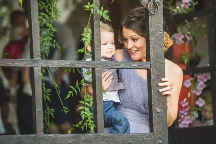 Bridesmaid in lilac holding a toddler behind an old window frame of ivy and flowers