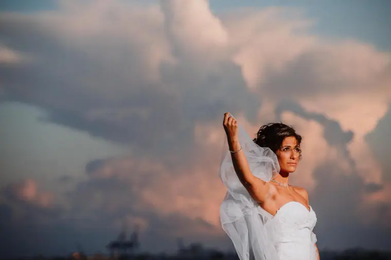 Bride raising her veil against a dramatic pink cloudy sky at Galu Seaside, Larnaca
