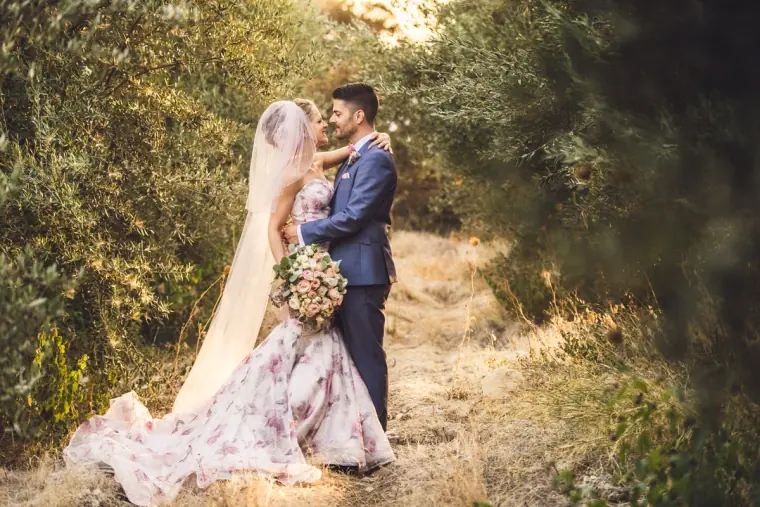 Bride in a floral gown embracing the groom on a shady woodland path