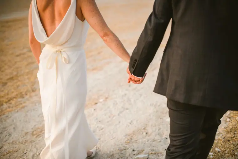 Close-up of the bride and groom holding hands as they walk, her gown's low back visible