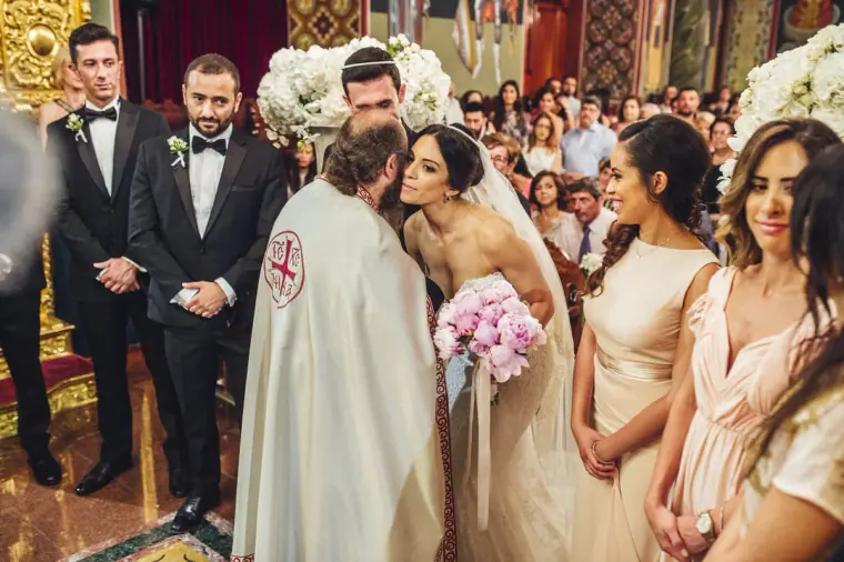 Bride kissing the priest's hand beside bridesmaids in blush dresses during the church ceremony