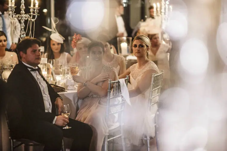 Guests at candlelit tables listening to speeches, seen through blurred crystal