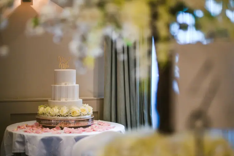 Three-tier white wedding cake on a petal-scattered table, glimpsed through blossoms