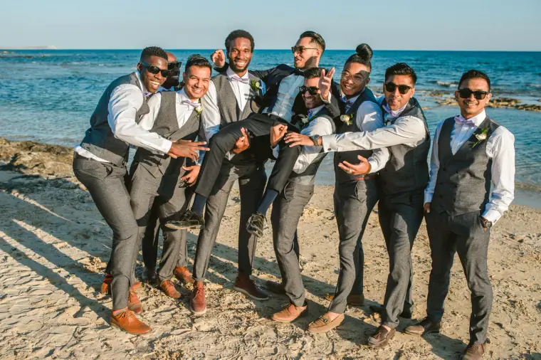 Groomsmen in grey waistcoats and sunglasses goofing around on the beach