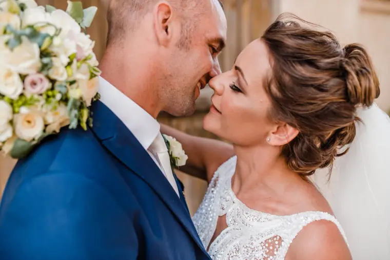Bride and groom about to kiss, a white rose bouquet against his shoulder