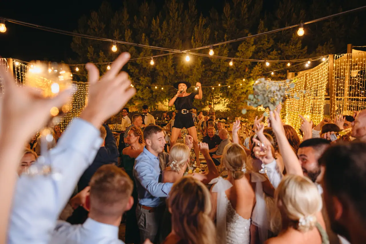 Guests dancing with hands in the air under festoon lights at night