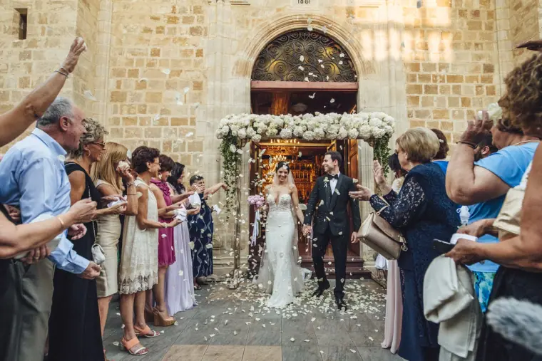 Guests throwing rice and petals as the newlyweds leave the church through a floral arch