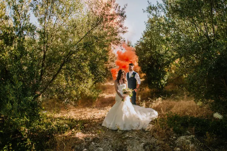 Orange smoke billowing behind the couple in a sunlit olive grove