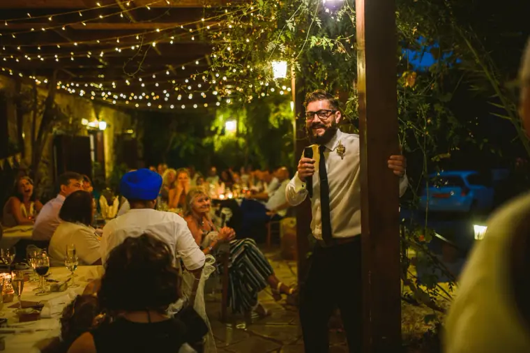 Man giving a speech beneath festoon lights at the evening reception