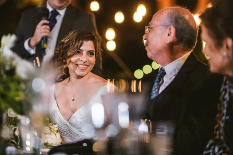 Bride smiling as a guest gives a speech at the reception