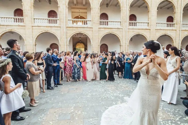 Bride turning to toss the bouquet in the courtyard, guests forming a wide circle