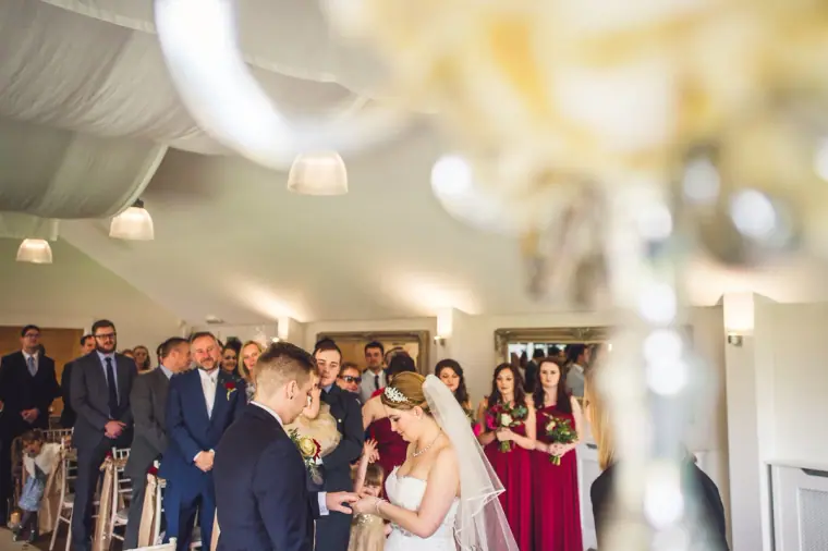 Ceremony room full of guests watching the couple, seen past a floral stand