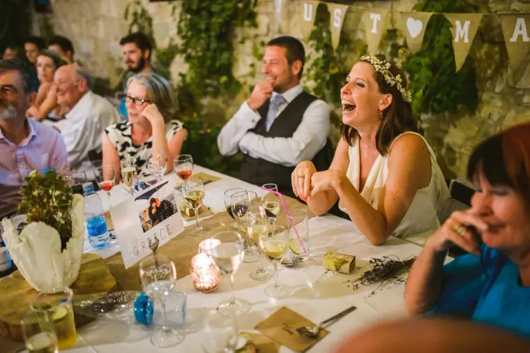 Bride laughing at the reception table as the groom smiles beside her