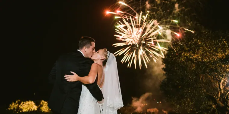 Bride and groom kissing as fireworks burst in the night sky
