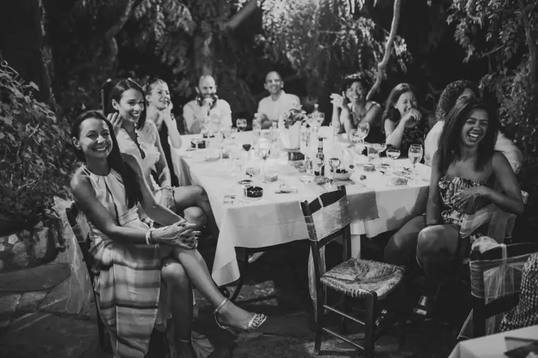 Black-and-white photo of guests laughing around a long candlelit table