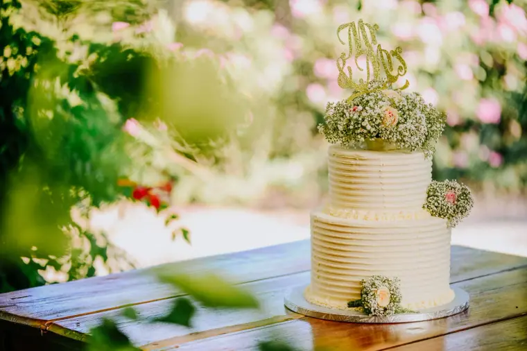 Three-tier white wedding cake with flowers and a gold topper on a rustic table