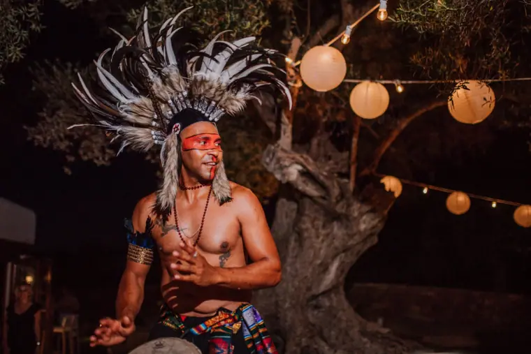 Performer in a feathered headdress and face paint dancing under festoon lights, Can Curreu, Ibiza
