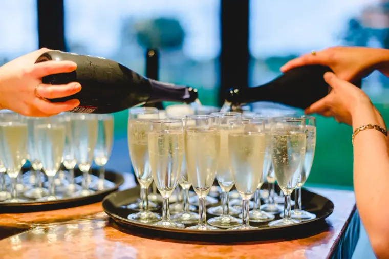 Waiters pouring champagne into rows of flutes on a tray