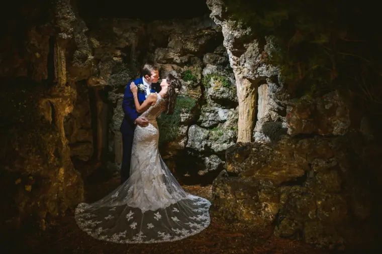 Iain and Elina embracing in the lit grotto, her lace train spread on the ground