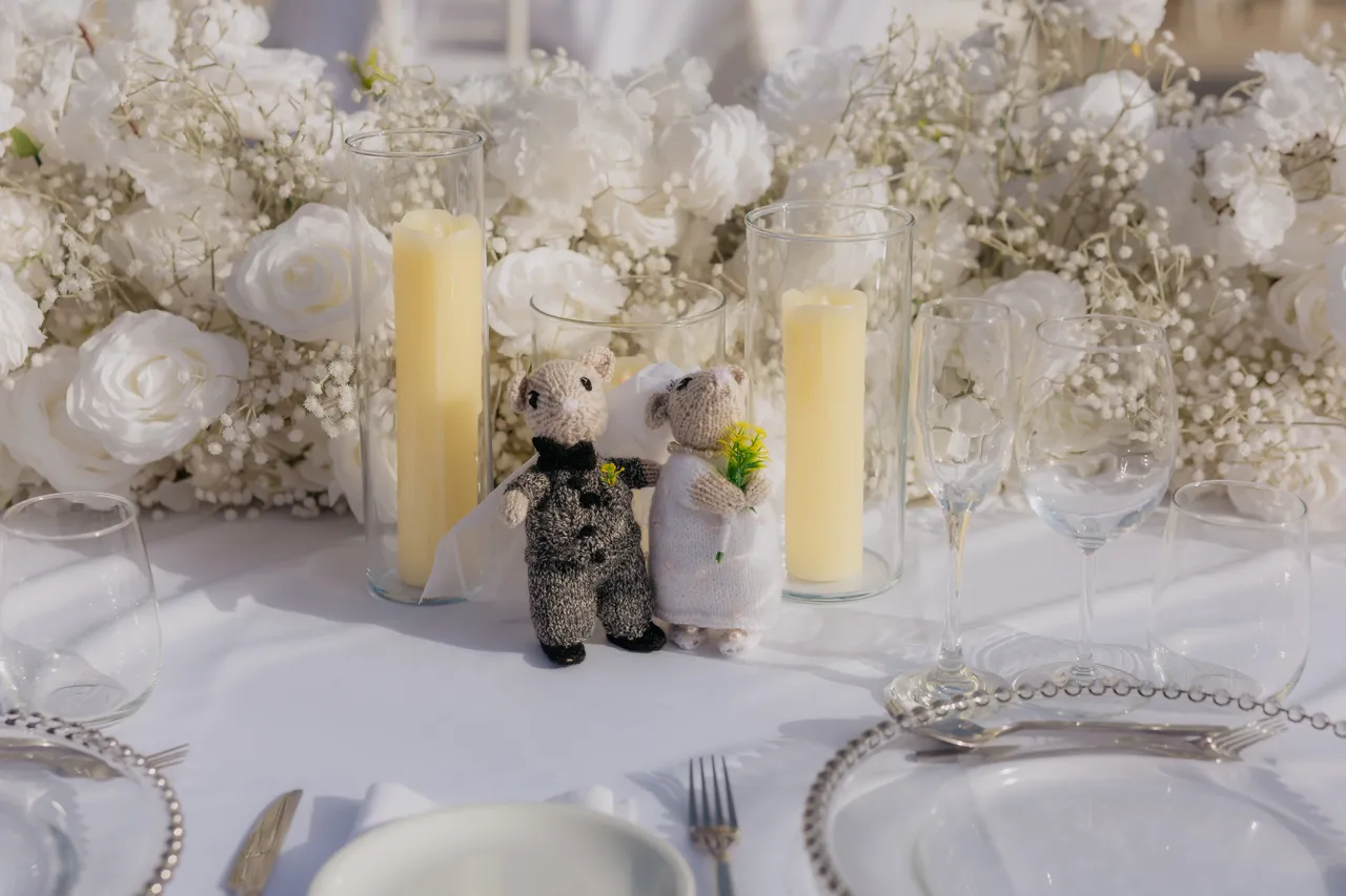 Small bride-and-groom figurines among white roses and candles on the top table