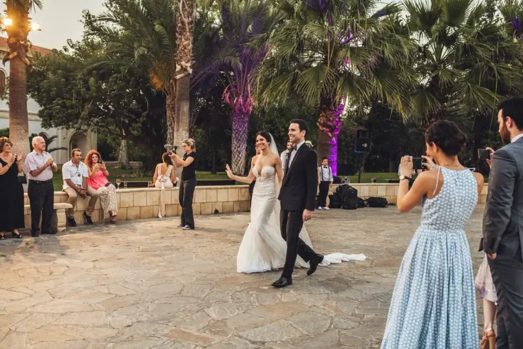 Newlyweds walking hand in hand across the terrace as guests take photos
