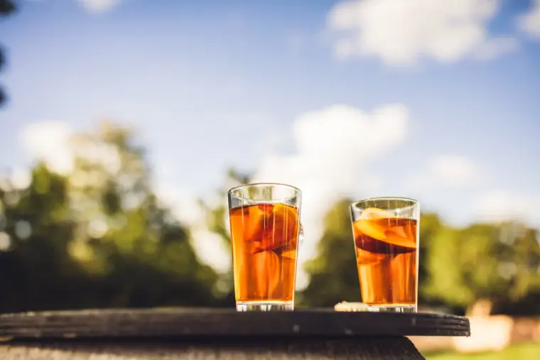 Two glasses of iced amber drinks with orange slices on a sunny table