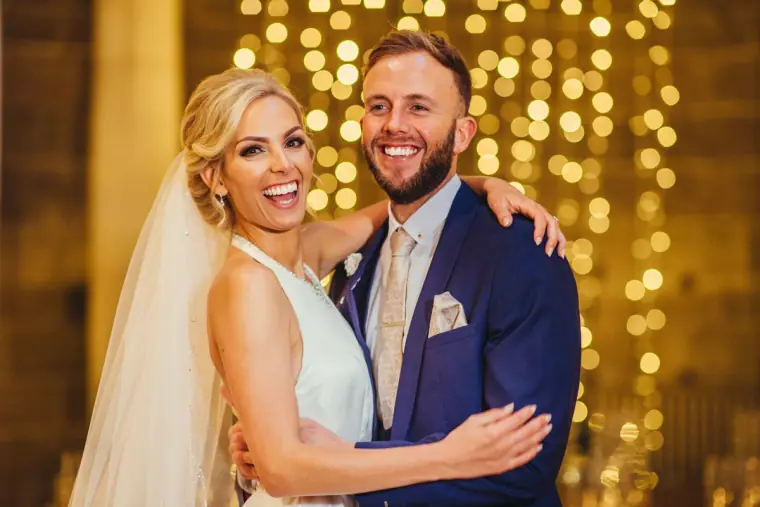 Bride and groom laughing together in front of golden fairy lights