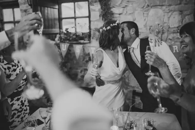 Black-and-white photo of the bride and groom kissing as guests raise their glasses