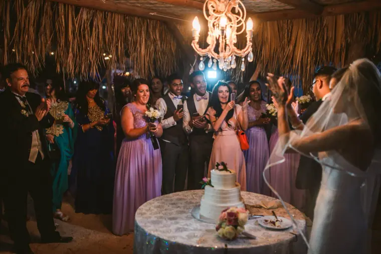 Guests gathered around the newlyweds for the cake cutting beneath a chandelier