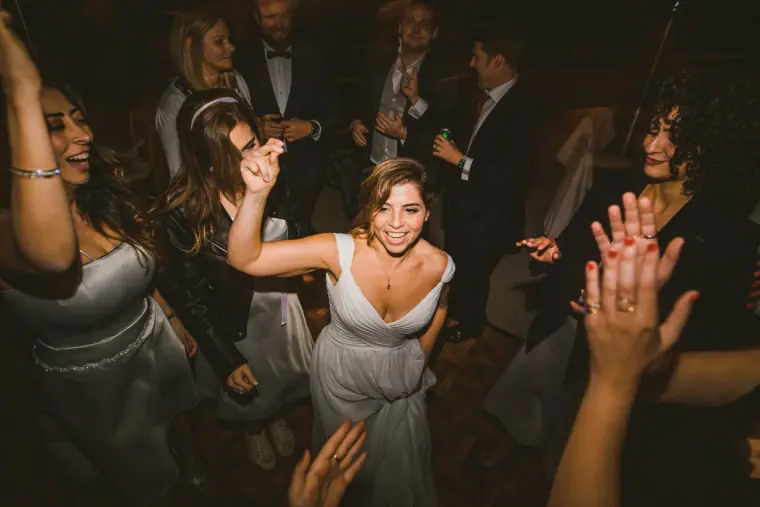 Bride dancing with arms raised among cheering guests and bridesmaids