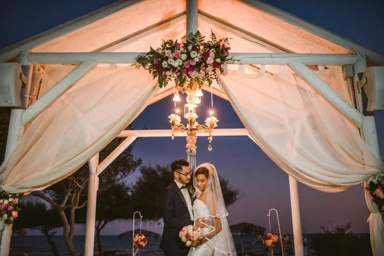 Bride and groom beneath the draped gazebo lit by a chandelier at dusk