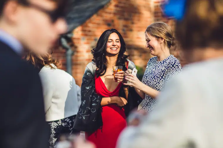 Guests laughing with drinks in the sunshine outside the barn