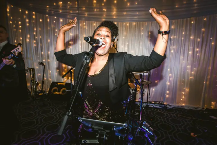 Singer performing with arms raised before a fairy-light curtain at the evening reception