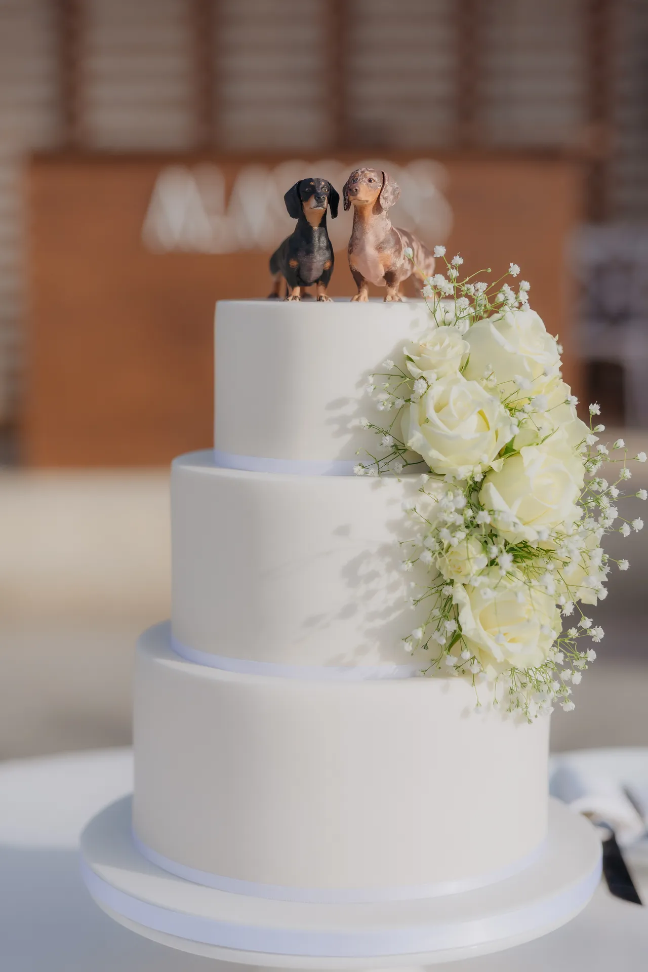 Three-tier white wedding cake with white roses and small dog figurines on top
