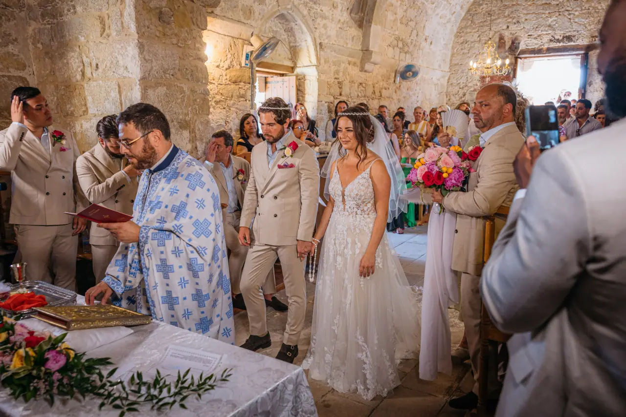 Orthodox priest in blue vestments leading Cliantha and Jack's ceremony in a stone church