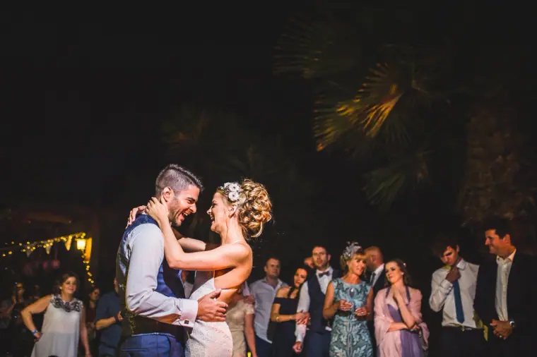 Groom laughing with the bride during their first dance as guests watch